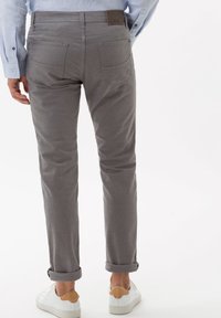 Chino grigi con vestibilità dritta, orli arrotolati, tasche posteriori e un'etichetta in pelle. Abbinati a sneakers bianche con accenti marroni.