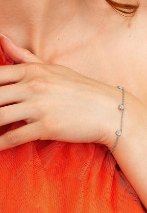 Zartes silbernes Kettenarmband mit zwei sternförmigen Diamantanhängern, getragen am Handgelenk über rotem Netzstoff.