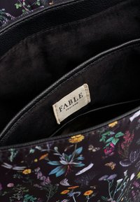 Unutrašnjost torbe s cvjetnim uzorkom s oznakom "FABLE" na tamnoj pozadini, koja prikazuje vibrantne ilustracije biljaka i insekata.