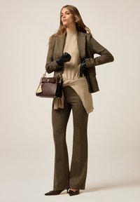 Blazer en tartan marron sur un haut en tricot beige, associé à un pantalon évasé à motifs marron. Gants en cuir noirs et un petit sac à main marron inclus.