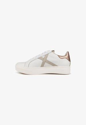 Zapatillas blancas con parte superior de cuero liso, con un detalle en el talón de color dorado metálico, diseño en cruz beige y una suela de goma blanca texturizada.