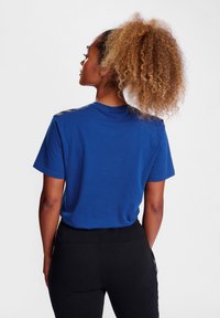 Blå bomulds t-shirt med korte ærmer, med sorte skulderdetaljer. Båret med sorte leggings, som viser en afslappet pasform og glat tekstur.