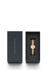 Roosa kuldne kell minimalistliku disainiga, ümmargune korpus ja ühendatud metallist käevõru, esitatud tumehallis karbis, mille sees on peen brändimine.