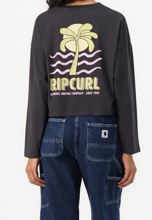 T-shirt court à manches longues noir avec motif palmier jaune et vagues roses, texte "Rip Curl Ultimate Surfing Company Since 1969" au dos.