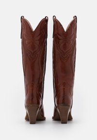 Botas de vaquero de cuero marrón con costuras intrincadas, cañas puntiagudas y tacón apilado. Superficie texturizada con acabado pulido.