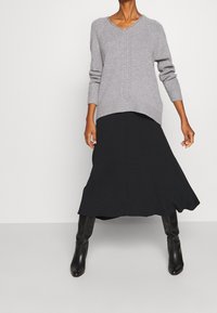 Harmaa neulepusero V-pääntiellä ja ribattuja hihansuita, yhdistetty mustaan keskipitkään hameeseen ja mustiin polvipitkiin saappaisiin.