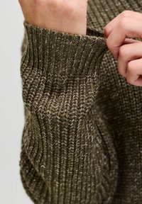 Strickpullover mit gerippten Bündchen in olivgrün. Der Stoff hat ein strukturiertes, dickes Erscheinungsbild mit hellen Akzenten durchgehend.