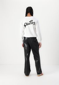 Schwarze, hoch taillierte Lederhosen mit glanzender Textur und zwei hinteren Taschen, kombiniert mit einem weißen Langarmshirt mit schwarzem Logo.