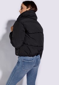 Chaqueta acolchada negra con cuello alto, que presenta un diseño de acolchados y un corte ligeramente corto, llevada sobre unos jeans de denim azul claro.
