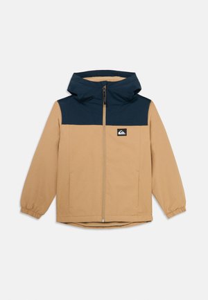 Veste beige pour enfants avec yoke bleu marine et capuche, fermeture éclair sur toute la longueur, poignets élastiques et patch logo sur la poitrine.