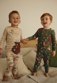 Pyjama rayé beige avec un graphisme du Gruffalo ; pyjama vert avec des motifs d'animaux de la forêt. Les deux sont fabriqués dans un tissu doux et possèdent des poignets et des chevilles élastiques.