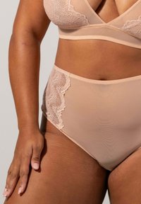Nude underklädesset med en mjuk bh i tyg med spetskant och höga trosor med spetsdetaljer på sidorna.