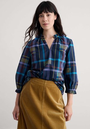 Marineblauwe geblokte blouse met blauwe, groene en bordeauxrode strepen; knoopsluiting, geraffineerde halslijn en lange mouwen met elastische manchetten. Te combineren met een corduroyrok.