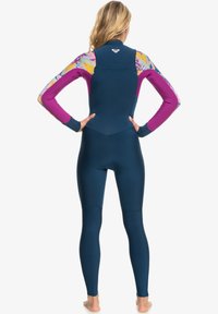 Un traje de neopreno que presenta un cuerpo de color azul oscuro y mangas con un vibrante estampado floral en rosa, púrpura y amarillo. El material parece flexible y tiene una textura suave.