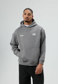 Grijze capuchontrui met een voorzak, geribbelde manchetten en gedurfde witte tekstgraphics. Gecombineerd met een zwarte broek.