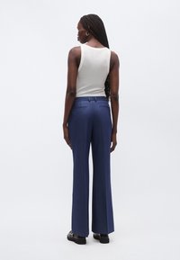 Tmavomodré nohavice so širokými nohavicami z textúrovanej látky s zadnými vreckami a hladkým pásom. Kombinované s priliehavým krémovým tielkom.