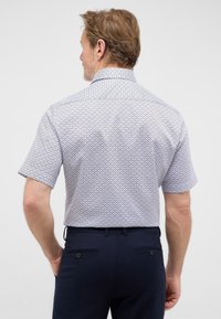 Hemd met korte mouwen voor heren in lichtblauw met een geometrisch patroon, voorzien van een klassieke kraag en een rugpand, gecombineerd met donkere broeken.
