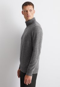 Maglione grigio a collo alto realizzato in tessuto a maglia strutturato, con colletto e orlo a coste, abbinato a pantaloni neri a righe.