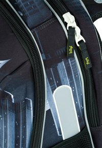 Schwarzer und grauer Rucksack mit grafischem Muster, ausgestattet mit Reißverschlussfächern, strukturiertem Stoff und gelben Logo-Akzenten.