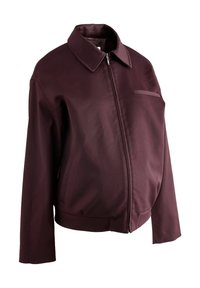 Burgundy bunda vyrobená z hladké tkaniny, s předním zipem, špičatým límcem, boční kapsou a uvolněným střihem s dlouhými rukávy.