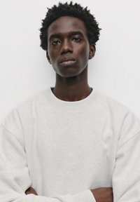 Sweatshirt gri deschis cu guler rotund și mâneci lungi, având o textură moale. Materialul pare puțin heathered.