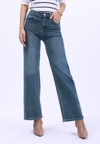 Jeans de mezclilla azul de pierna ancha con cintura alta, que cuentan con bolsillos frontales, cierre de botón y detalles de desgaste sutil.