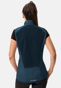 Mørkeblå vest med høy krage, lett materiale, mesh-paneler og logo på baksiden. Glatt tekstur med en tettsittende design.