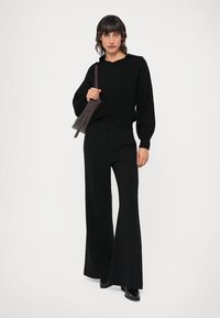 Fekete kötött pulóver laza szabással, párosítva elegáns fekete, bő szárú nadrággal és egy letisztult, sötét táskával.