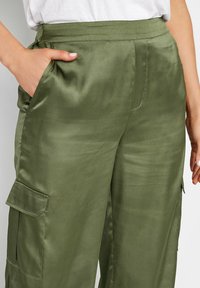 Olijfgroene satijnen cargo-broek met een gladde textuur, zijzakken en een elastische tailleband. Heeft een relaxte pasvorm en verfijnde details.