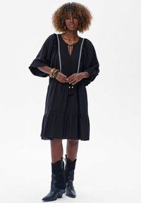 Zwarte jurk met pofmouwen, een V-hals en witte details. Heeft een gelaagde rok en franjes bij de halslijn. Gekocht met zwarte laarzen.