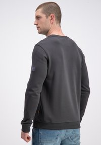 Ciemnoszara bluza z okrągłym dekoltem i ściągaczami na rękawach, z naszywką z logo na lewym rękawie i luźnym krojem.