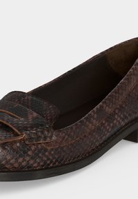 Mocassin en cuir marron texturé avec un petit talon et des détails de couture apparents sur le dessus avant.