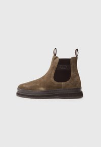 Brown suede Chelsea boot featuring elastic side panels, pull tab, and a thick, textured rubber sole with subtle grooves for grip.
