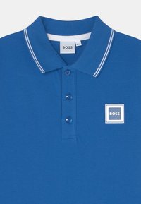 Polo shirt blu realizzato in tessuto testurizzato, con colletto classico, tre bottoni e un'etichetta quadrata con logo bianco e blu navy.