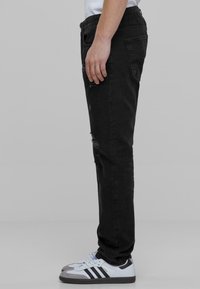 Mustat farkut slim fit -mallilla, joissa on kulutustekstuureja ja klassinen 5-taskuinen muotoilu. Yhdistettynä valkoisiin ja harmaisiin lenkkarit.