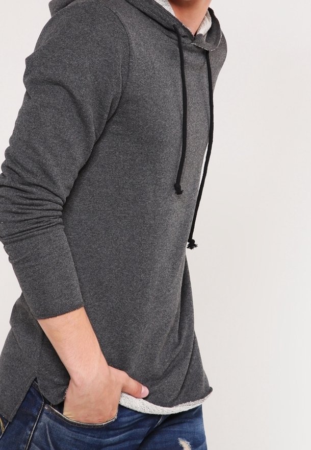 Felpa grigia con maniche lunghe, cappuccio con cordino e fessure laterali. Realizzata in tessuto morbido, presenta un orlo interno testurizzato. Indossata con jeans blu.