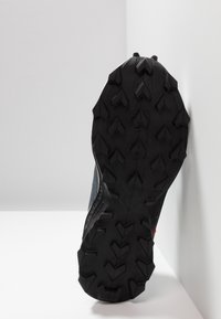 Zwarte rubberen schoenzool met diepe profielpatronen; textuurafwerking; gedeeltelijk zichtbaar grijs bovenmateriaal en ontwerpcontouren.