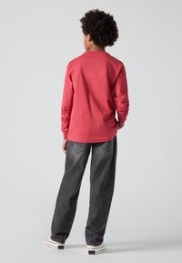 Camiseta de algodón roja de manga larga combinada con pantalones de denim gris. El conjunto incluye pantalones de corte relajado y zapatillas blancas con acentos negros.