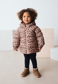 Geacă matlasată roz cu imprimeu leopard și glugă, cu manșete elastice și fermoar frontal, purtată peste colanți negri și cizme cu imprimeu leopard.