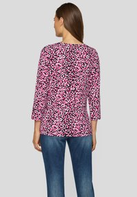Long-sleeve shirt in a pink and black leopard print design, featuring a rounded neckline and relaxed fit. Worn with blue jeans.