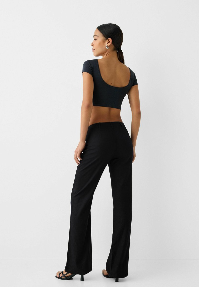 Schwarze weit geschnittene Hosen kombiniert mit einem enganliegenden dunklen Oberteil mit tiefem Rückenausschnitt, glattem Stoff und minimalem Design.