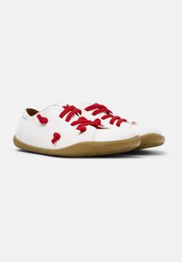 Bottes en cuir blanc avec des lacets et des accents rouges, dotées d'une semelle en caoutchouc brun texturé. Forme arrondie avec des détails de couture sur le dessus.
