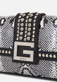 Bolso de mano con textura de piel de serpiente en blanco y negro, que cuenta con una correa de cuero negro adornada con clavos plateados y una hebilla de logo G con joyas.