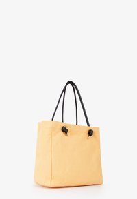 Borsa a tote gialla in tela con manici in pelle nera, caratterizzata da dettagli annodati e una forma strutturata, adatta all'uso quotidiano.