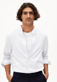 Weißes Baumwollhemd mit Knöpfen und Stehkragen, hochgerollten Ärmeln und feinen Nähten, über einem weißen Rundhals-T-Shirt getragen.