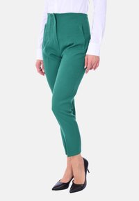 Pantaloni verde a vita alta con pieghe, dotati di tasche laterali, abbinati a tacchi neri a punta. Tessuto morbido e vestibilità sartoriale.