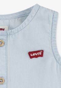 Ljusblå ärmlös plagg med rund halsringning och knappstängning, med en röd broderad Levi's-logotyp på bröstet. Texturerat tyg.