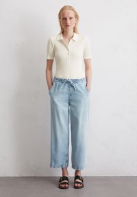 Ribbed, short-sleeve polo in light cream with a button placket, paired with light blue, wide-leg denim pants and black sandals with a buckle.
