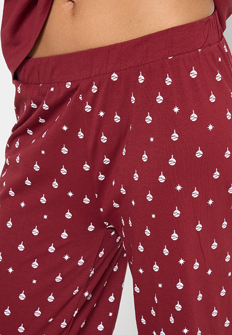 Rode pyjamabroek gemaakt van zachte stof, voorzien van een herhaald patroon van witte ornamenten en sterren, met een elastische tailleband voor comfort.