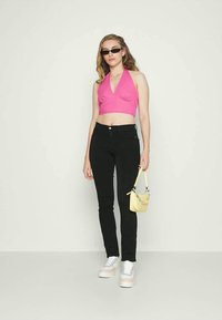 Top cropped halter cor-de-rosa com detalhes franzidos, combinado com jeans pretos de cintura alta. Acessórios incluem uma pequena bolsa amarela e tênis brancos.